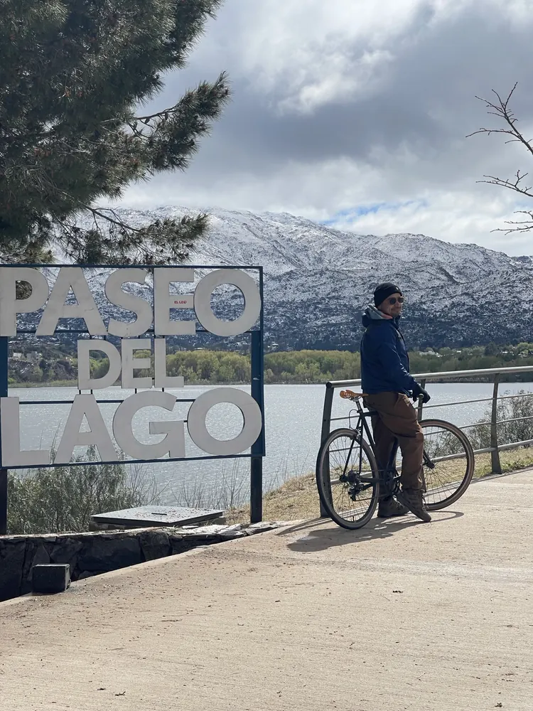 Ciclista con su bici en el Paseo del Lago de Potrero de los Funes, con las sierras nevadas de fondo